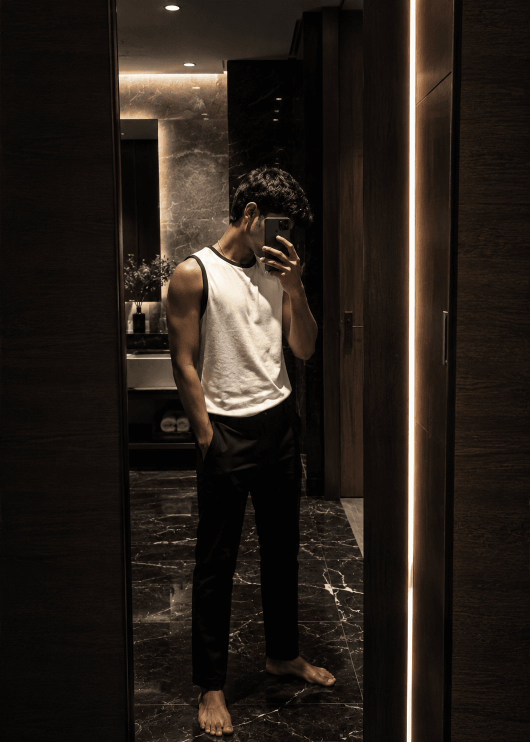 Low-light mirror portrait in a dark marble interior lit by a single warm strip light