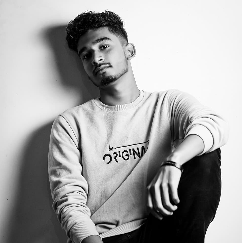 Black and white studio portrait leaning against a bare wall in a "be original" sweatshirt