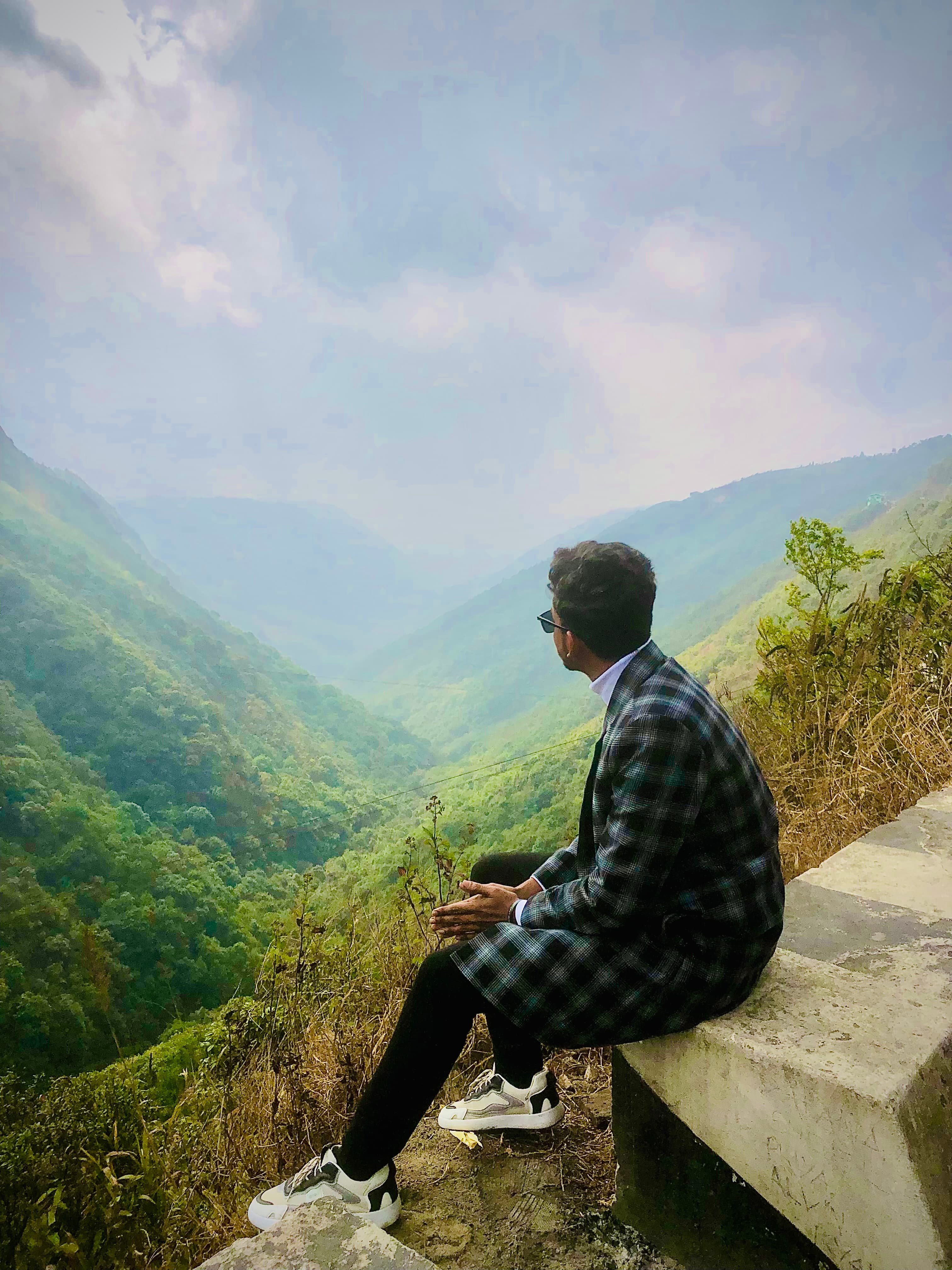 Sitting on a roadside ledge above a green valley of mist-covered hills